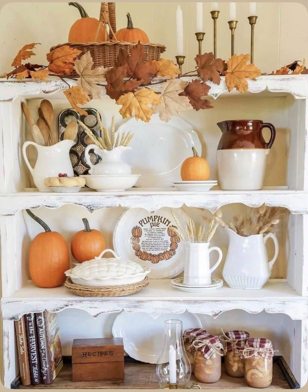 White hutch with pumpkins, white dishes, and autumn leaves