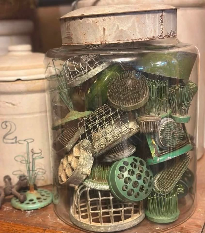 A glass jar filled with vintage metal flower frogs in varied shapes and green patinas