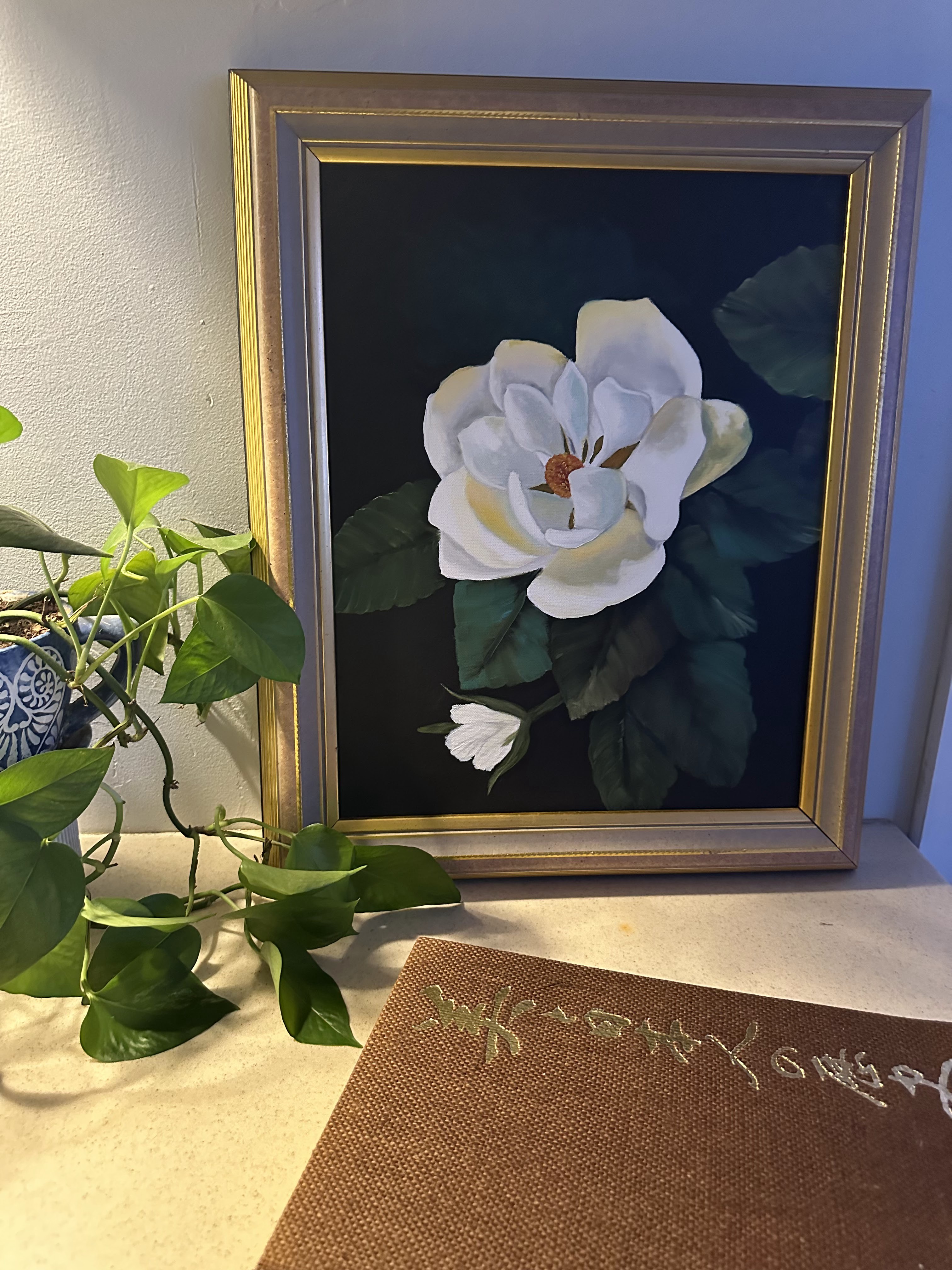 Thrifted magnolia artwork in a gold frame beside a houseplant