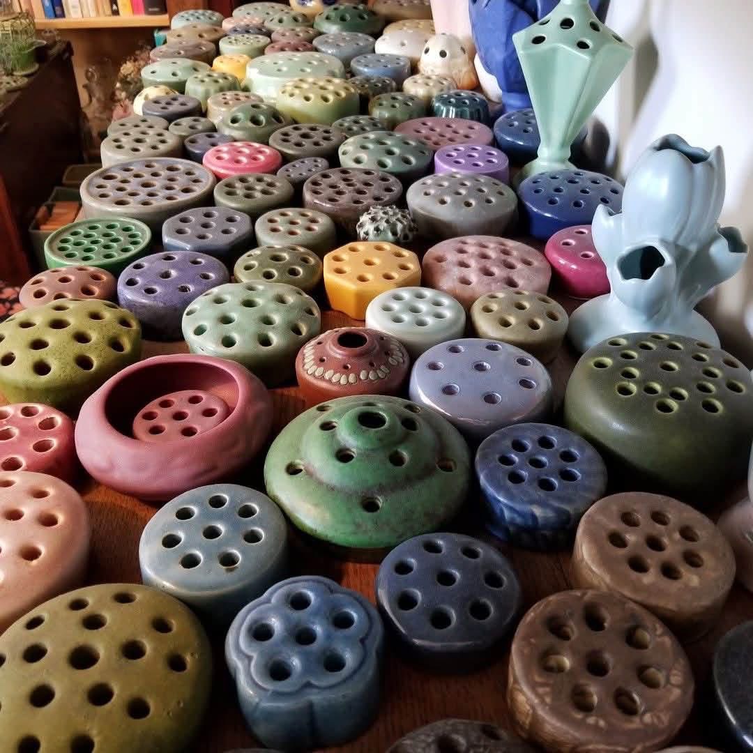 A large collection of ceramic flower frogs in varied colors and forms