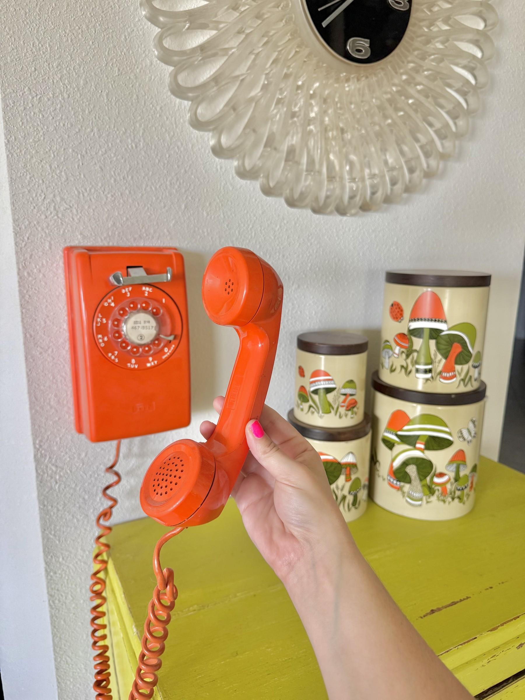 An orange rotary phone and handset beside vintage mushroom canisters in our kitchen