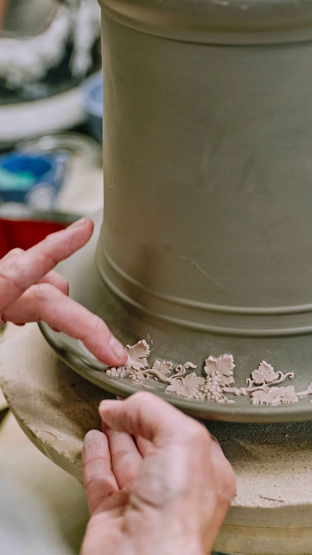 Hands applying raised pale vine decoration to a green pottery vessel