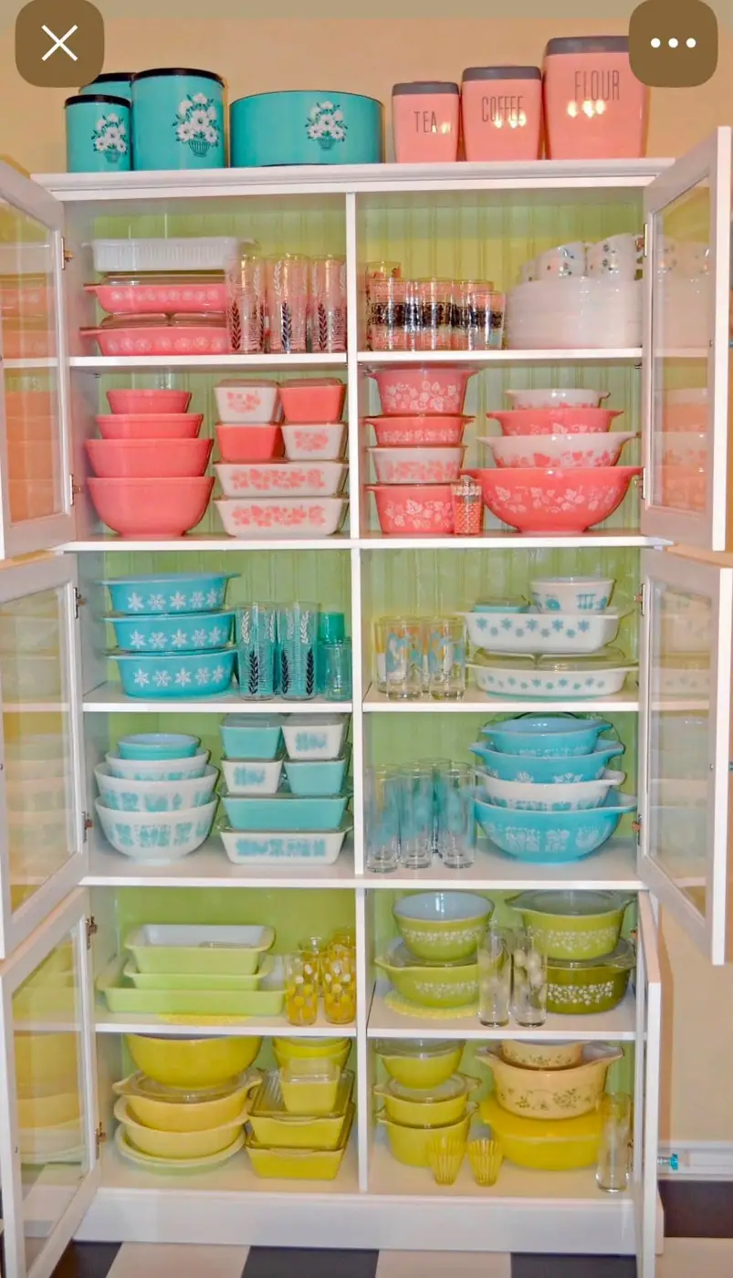 Pink turquoise and yellow Pyrex arranged in a tall white cabinet