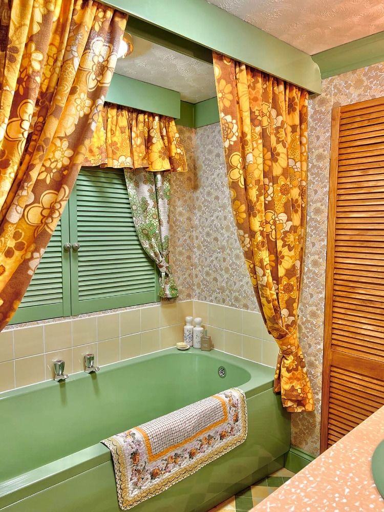 Green bathtub framed by golden floral curtains
