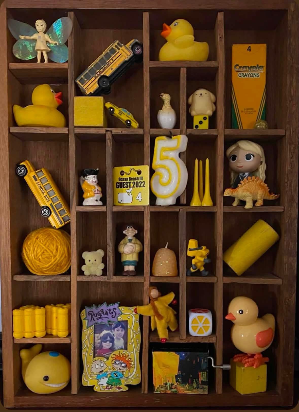 Yellow miniature objects displayed in wooden compartments