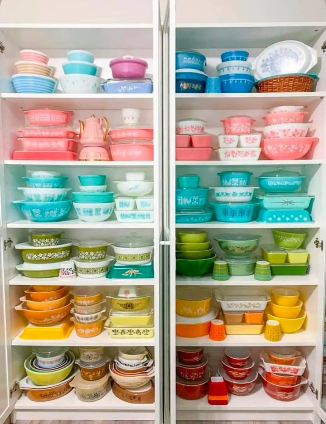 Rainbow Pyrex collection arranged by color in a white cabinet