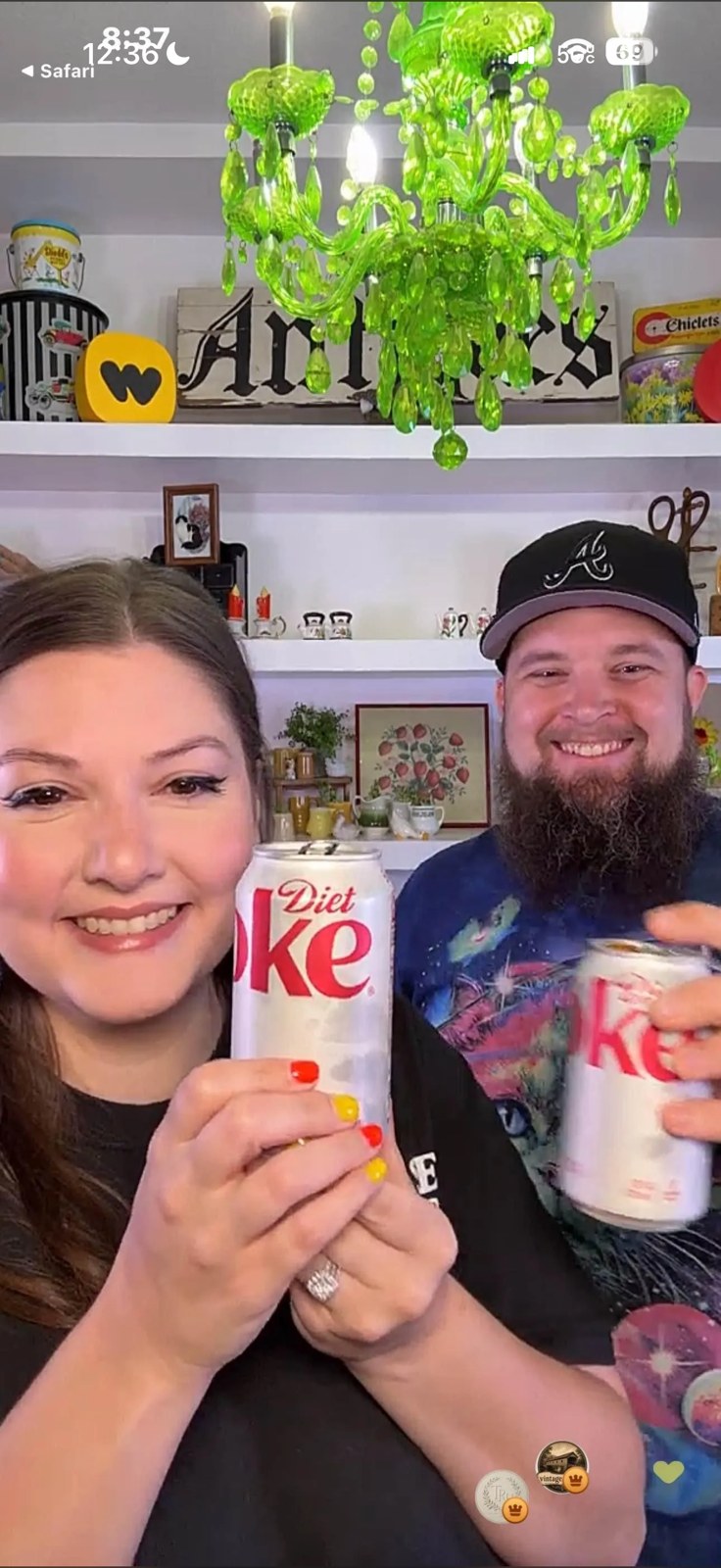 Ashley and Jacob raising Diet Coke cans in their studio beneath the green chandelier