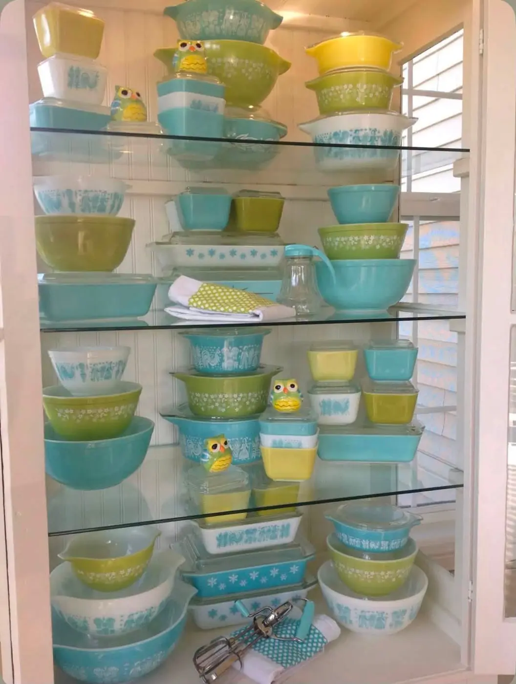 Turquoise and green Pyrex with small owl decorations in a glass cabinet