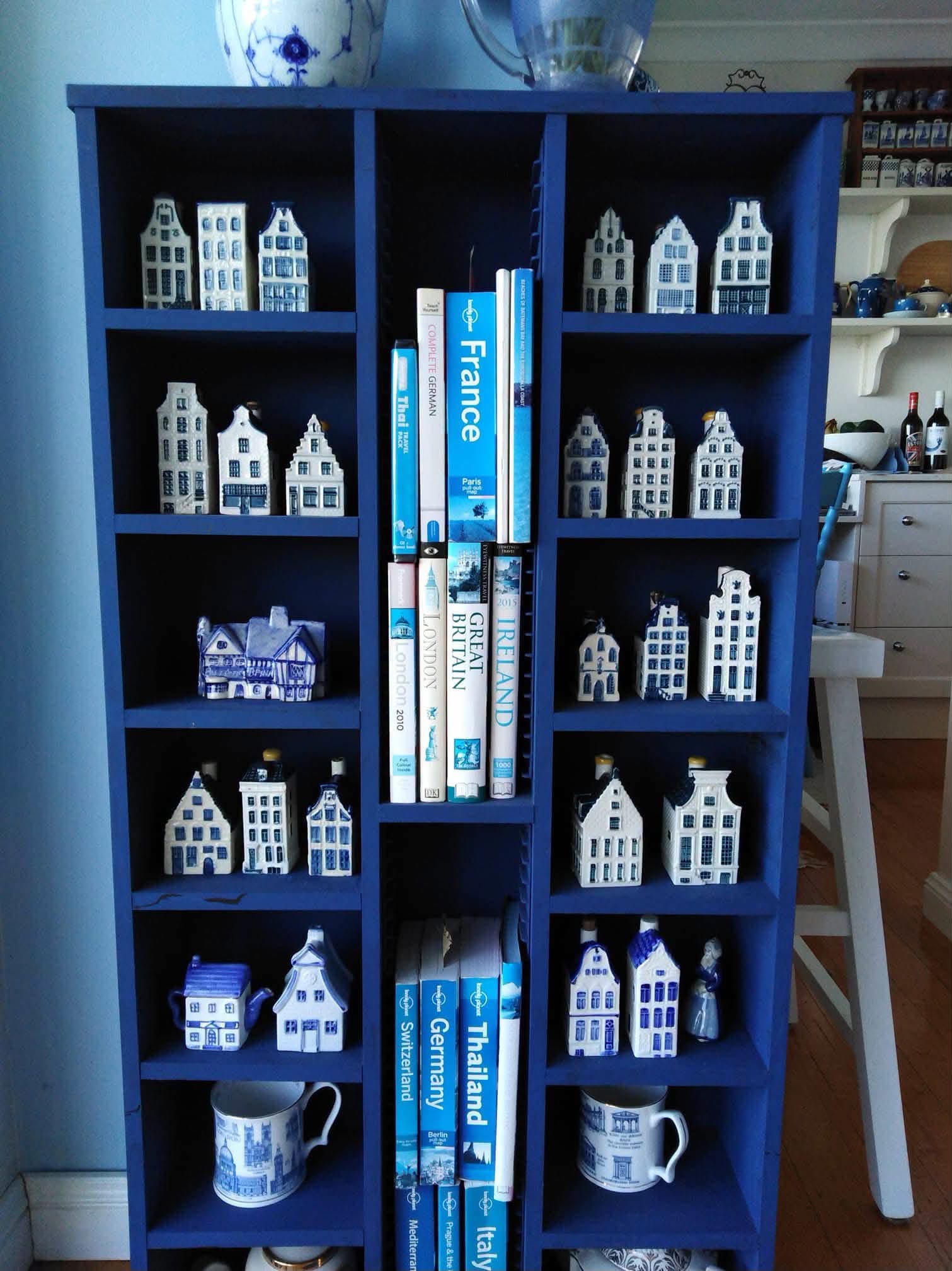 Blue shelving displaying miniature Delft houses alongside travel books