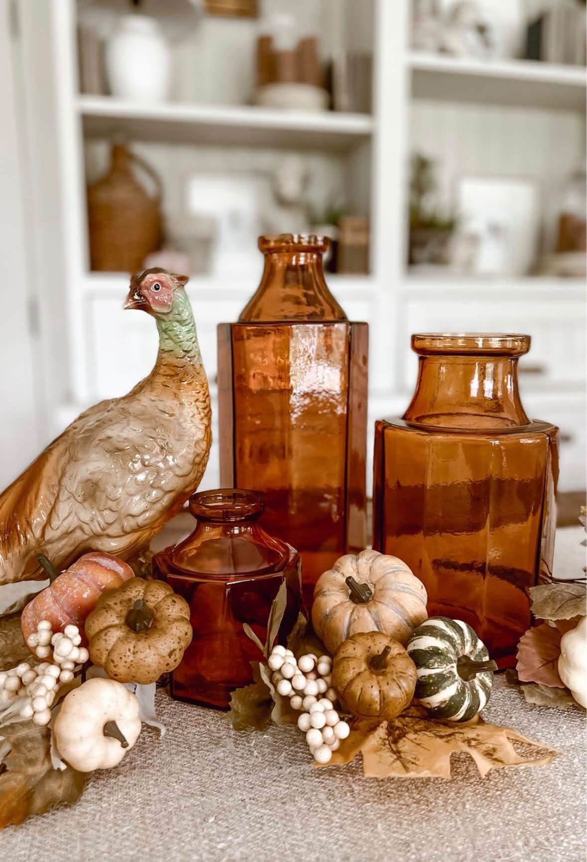 Amber glass bottles, a ceramic pheasant, and small pumpkins arranged for fall