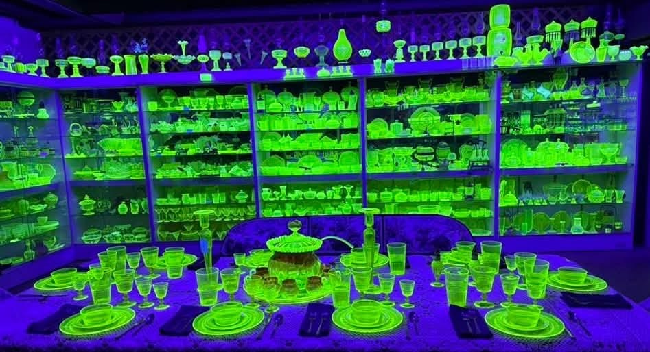 Glowing green vintage glass displayed across shelves and a dining table under ultraviolet light