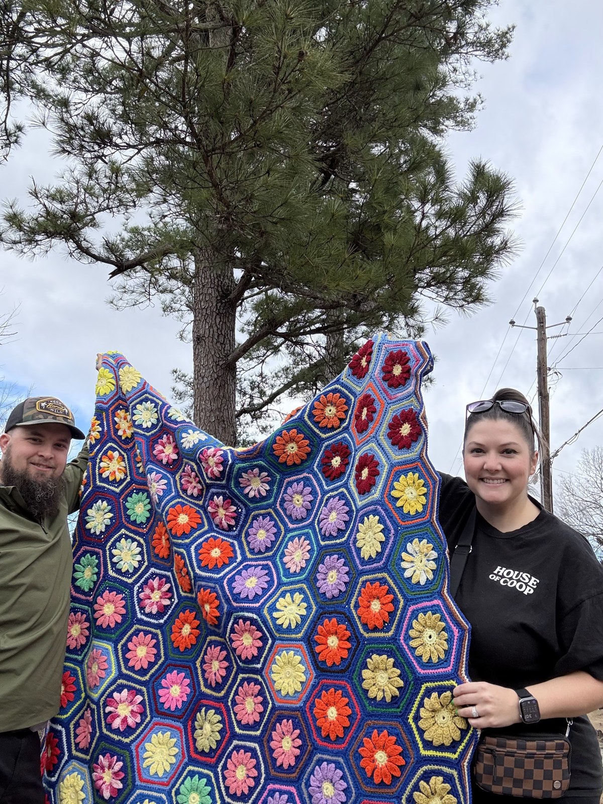 Ashley and Jacob holding up a colorful crocheted blanket outdoors