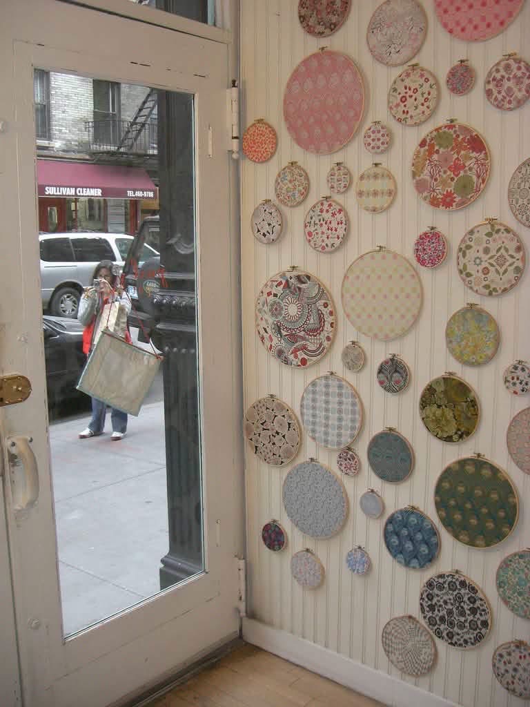 Patterned fabric displayed in embroidery hoops beside a shop door
