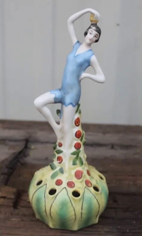 A ceramic flower frog featuring a woman in a blue outfit
