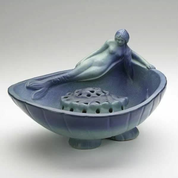 A blue ceramic bowl and flower frog with a reclining figure