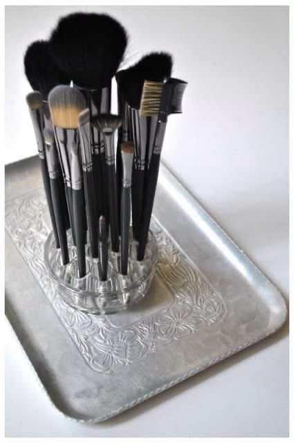 Makeup brushes organized in a glass flower frog on a silver tray