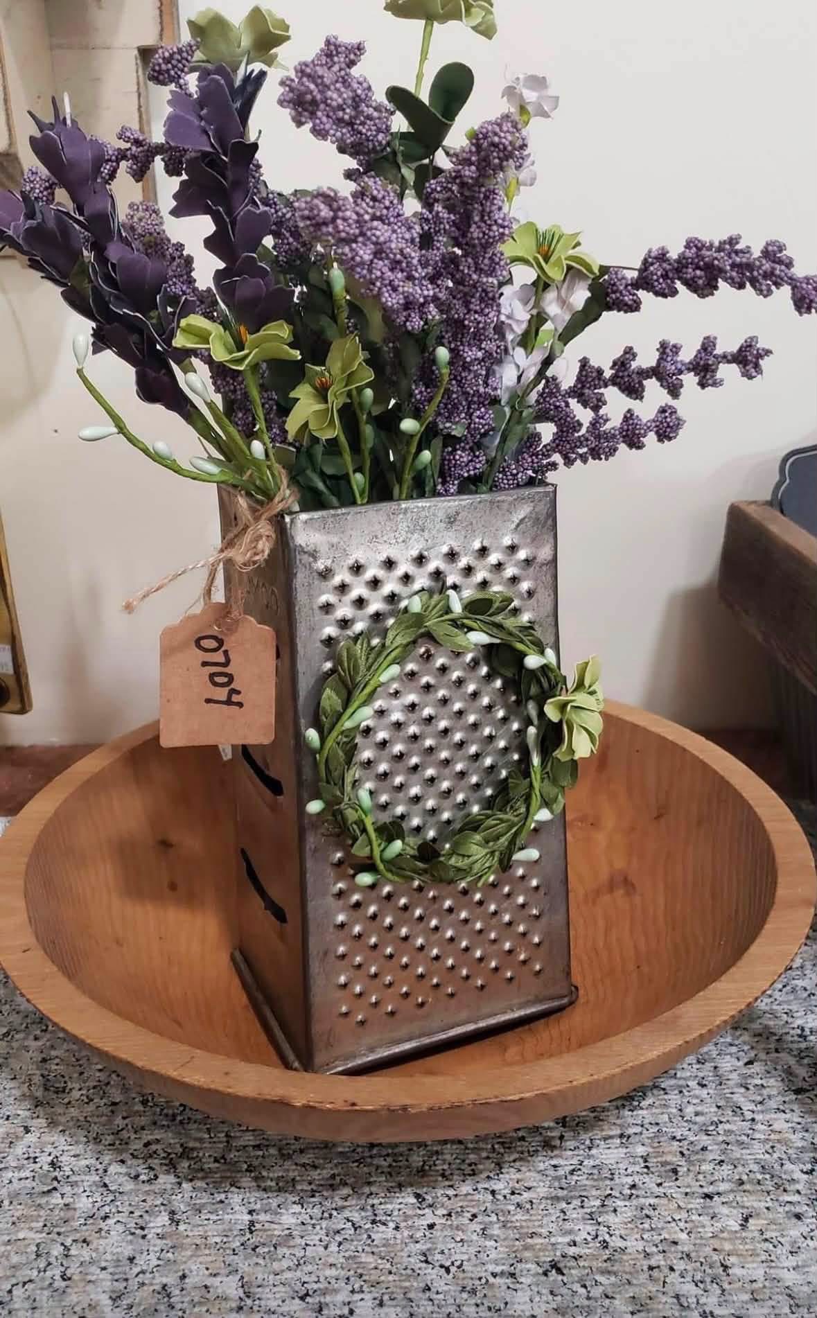 Purple floral stems in a vintage box grater inside a wooden bowl