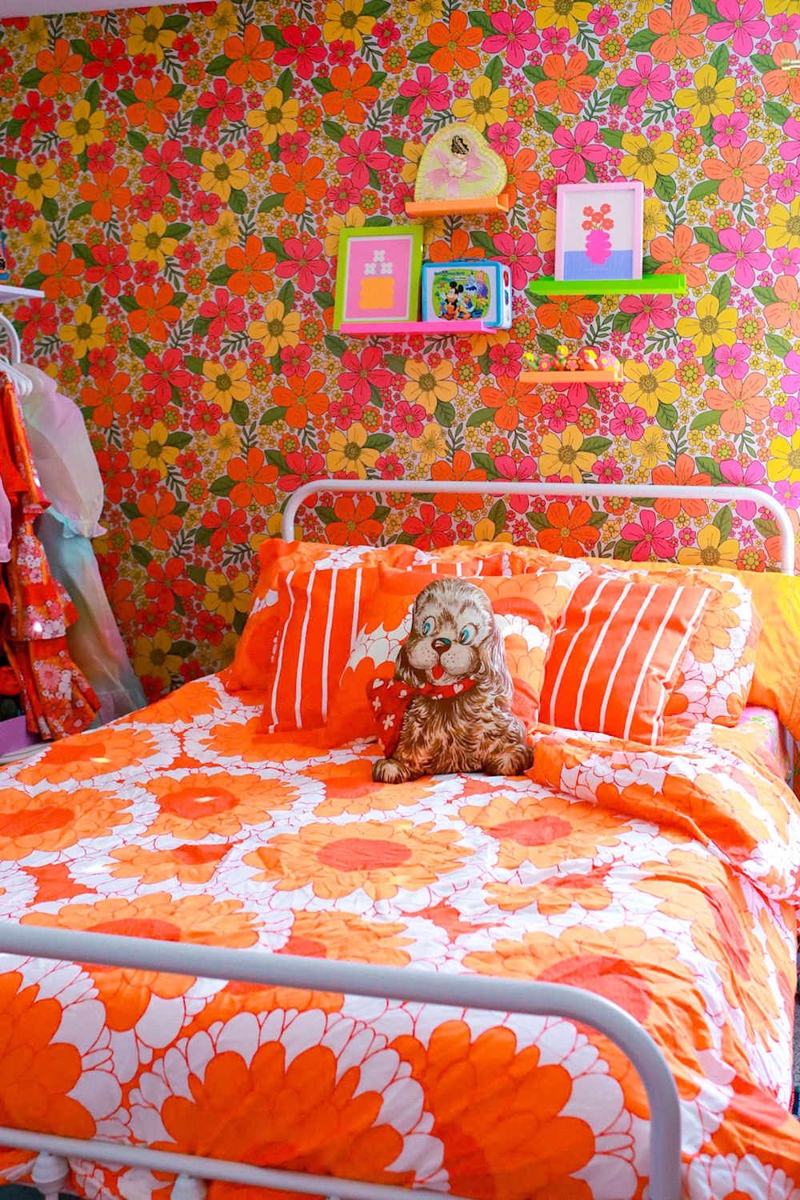 Orange floral bedding beneath vibrant floral wallpaper