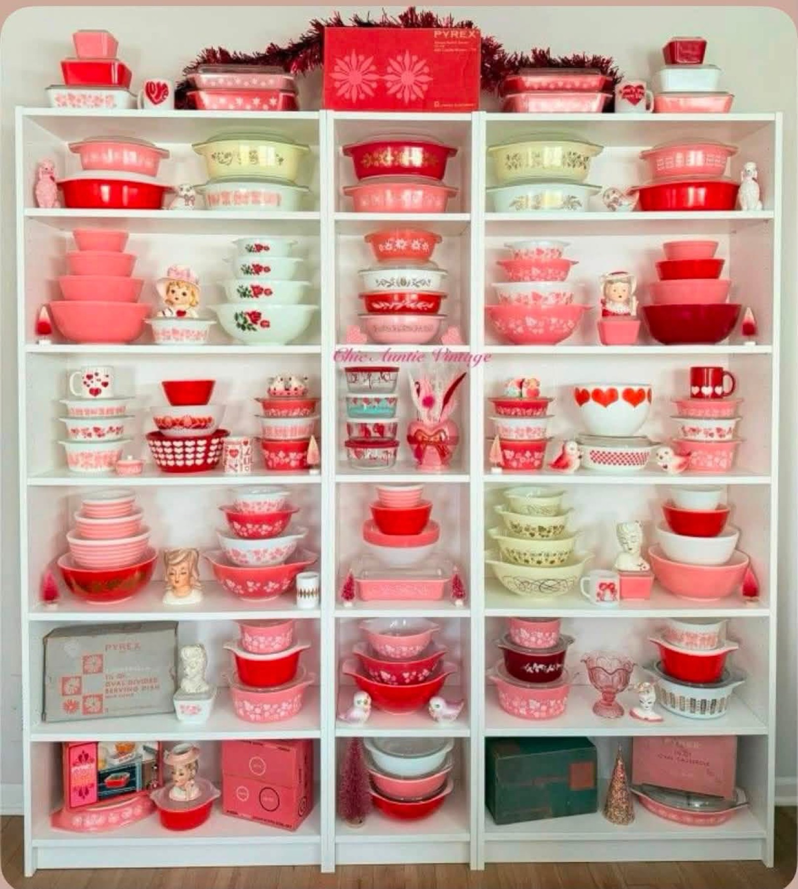 Pink, red, and pale green vintage Pyrex arranged across white display shelves
