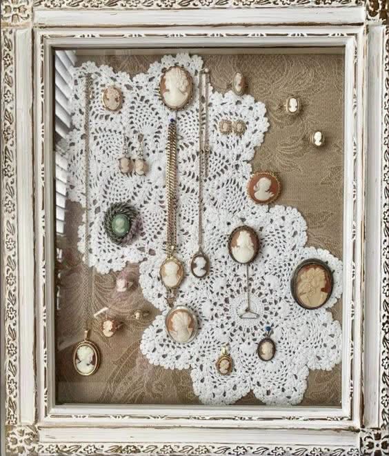 Cameo jewelry displayed on doilies in an ornate white frame