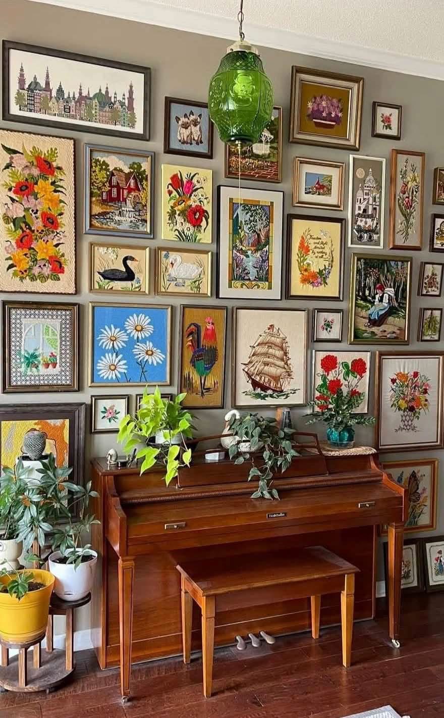 Needlepoint and crewel pictures above a piano with plants