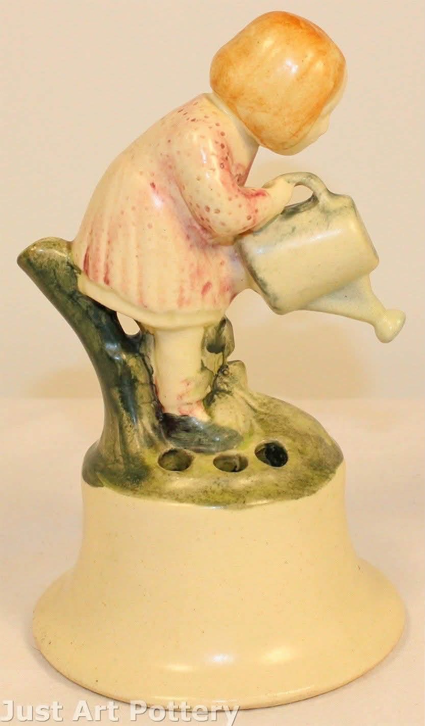A ceramic flower frog featuring a child with a watering can