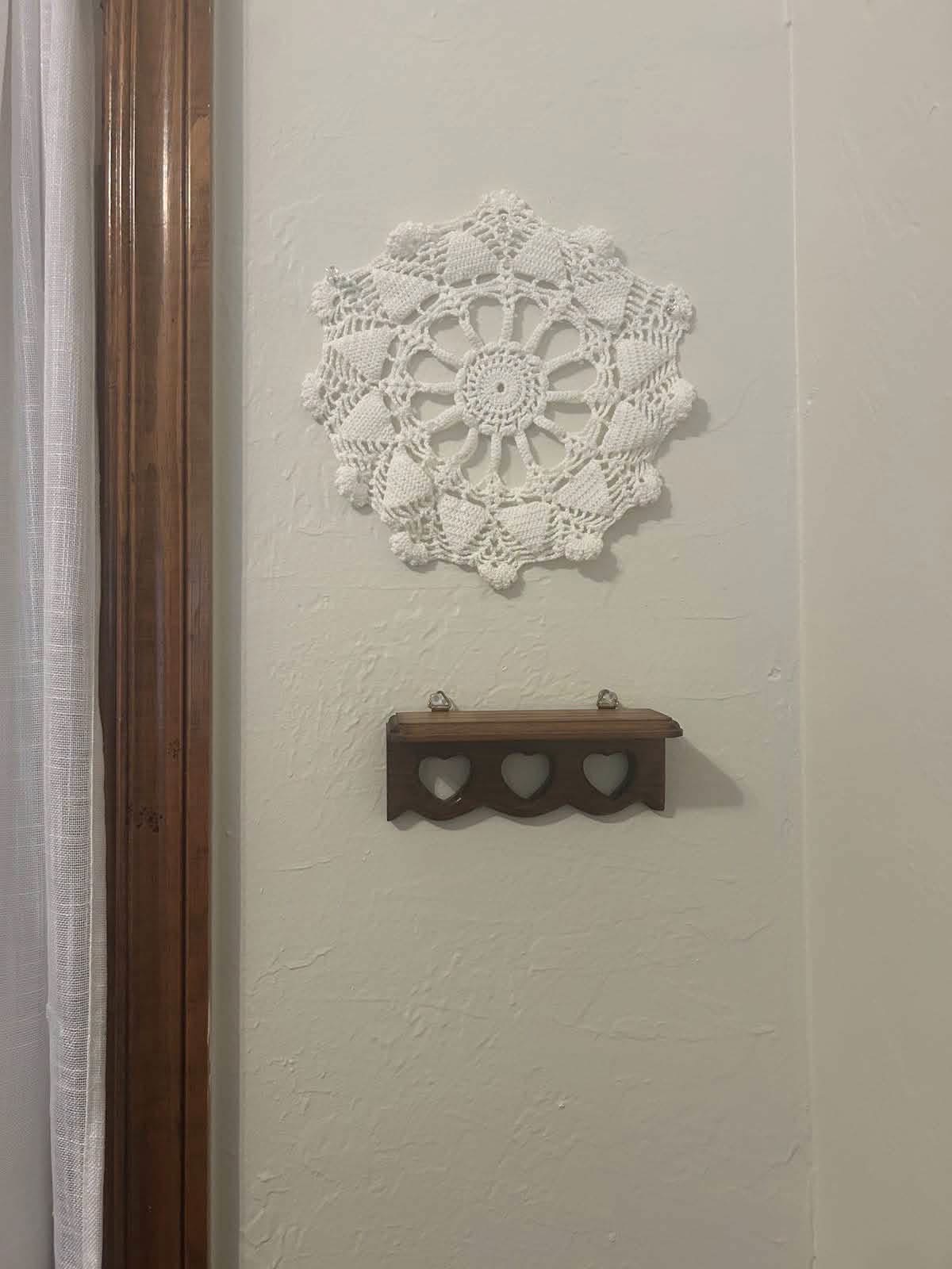A single white doily on the wall above a small wooden shelf