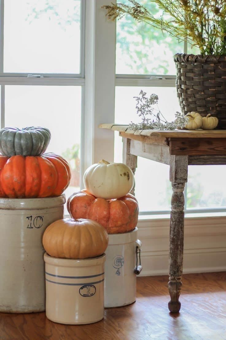 Pumpkins stacked on stoneware crocks beside a wooden table