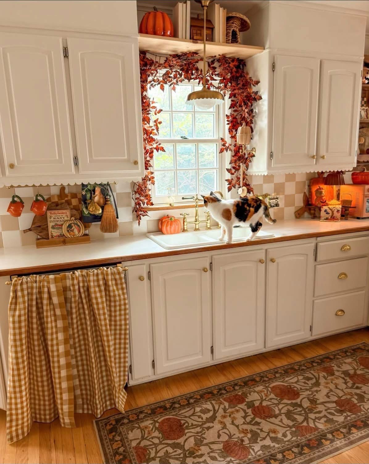 Autumn kitchen with leaf garland, pumpkins, and a cat by the sink