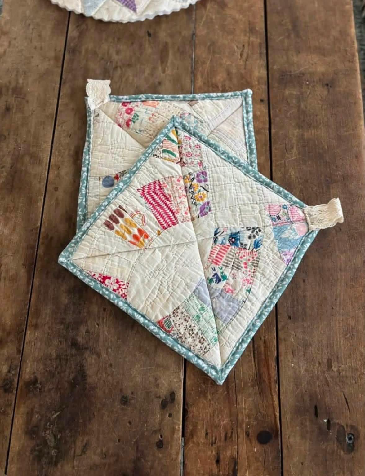 Two quilted potholders with teal edging on a wooden table