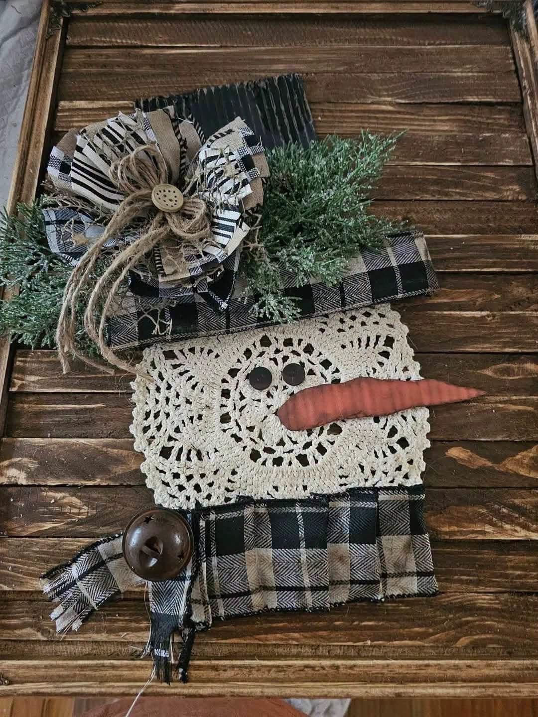 A snowman decoration made from a doily with a checked hat and scarf