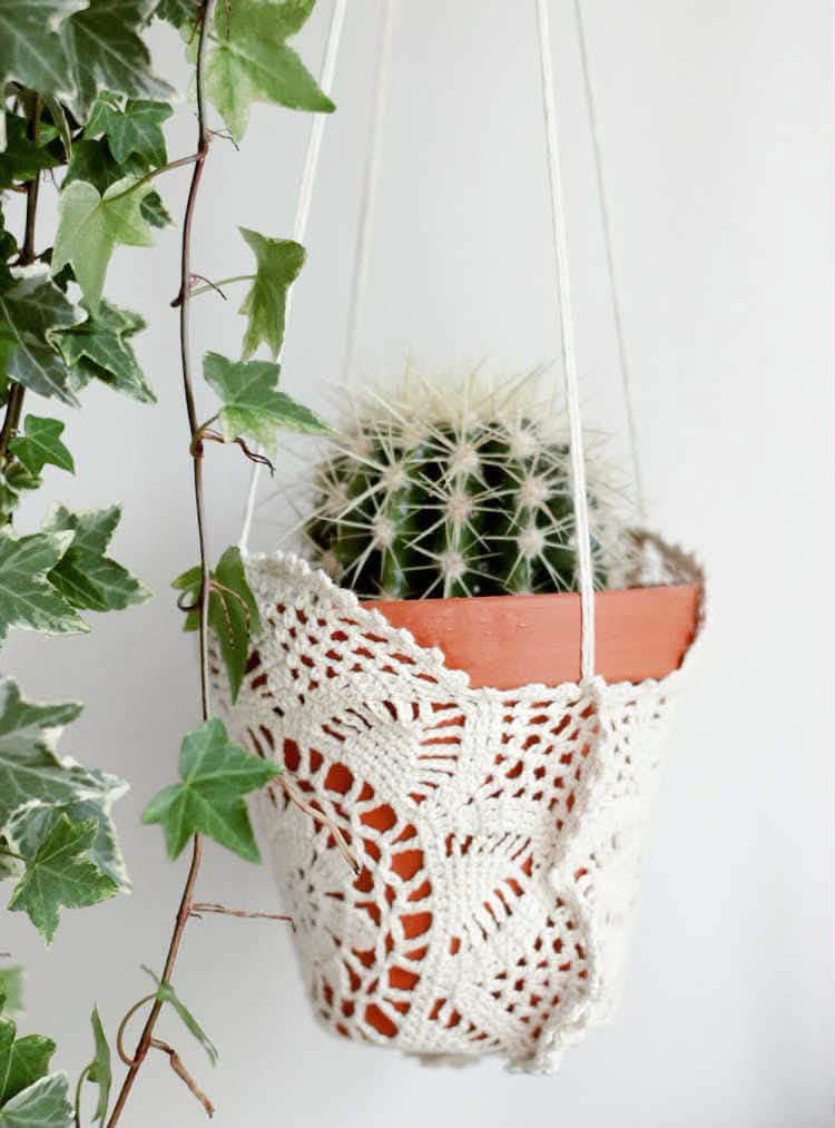 A terracotta cactus pot suspended in a crocheted doily hanger