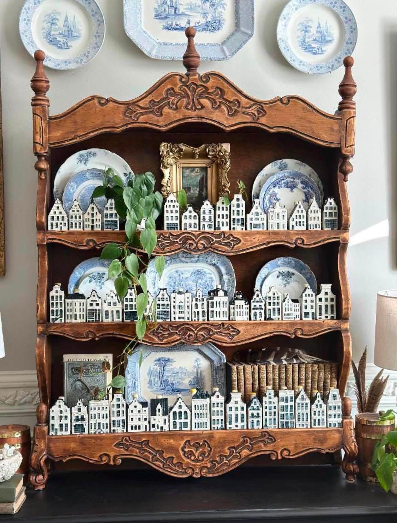 Miniature Delft houses and blue and white plates displayed on an ornate wooden hutch
