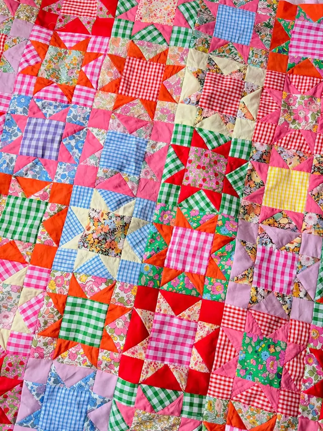 Colorful vintage star patchwork quilt with gingham and floral fabrics in pink, red, green, blue and yellow