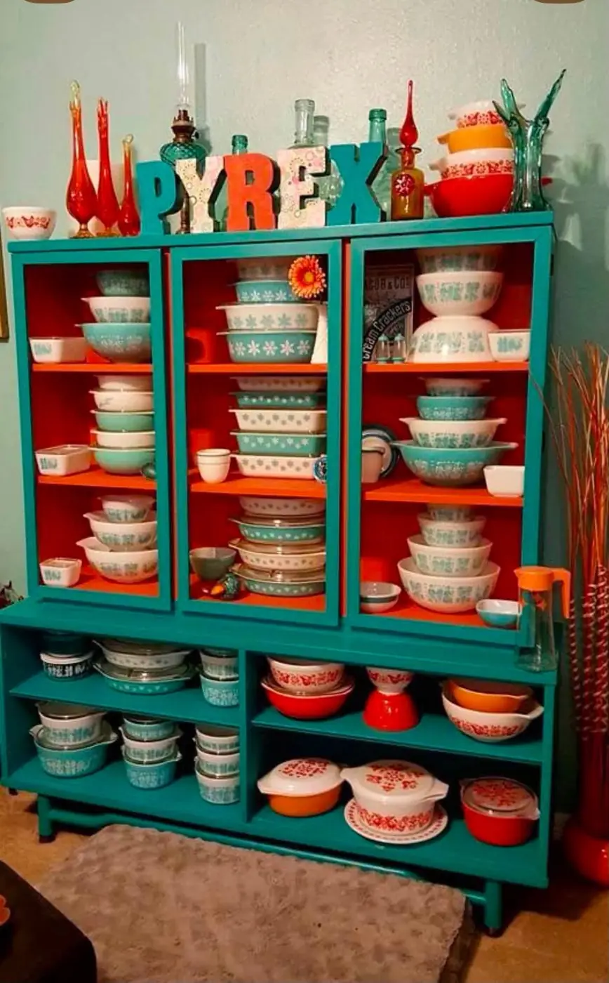Turquoise cabinet with orange shelves filled with patterned Pyrex