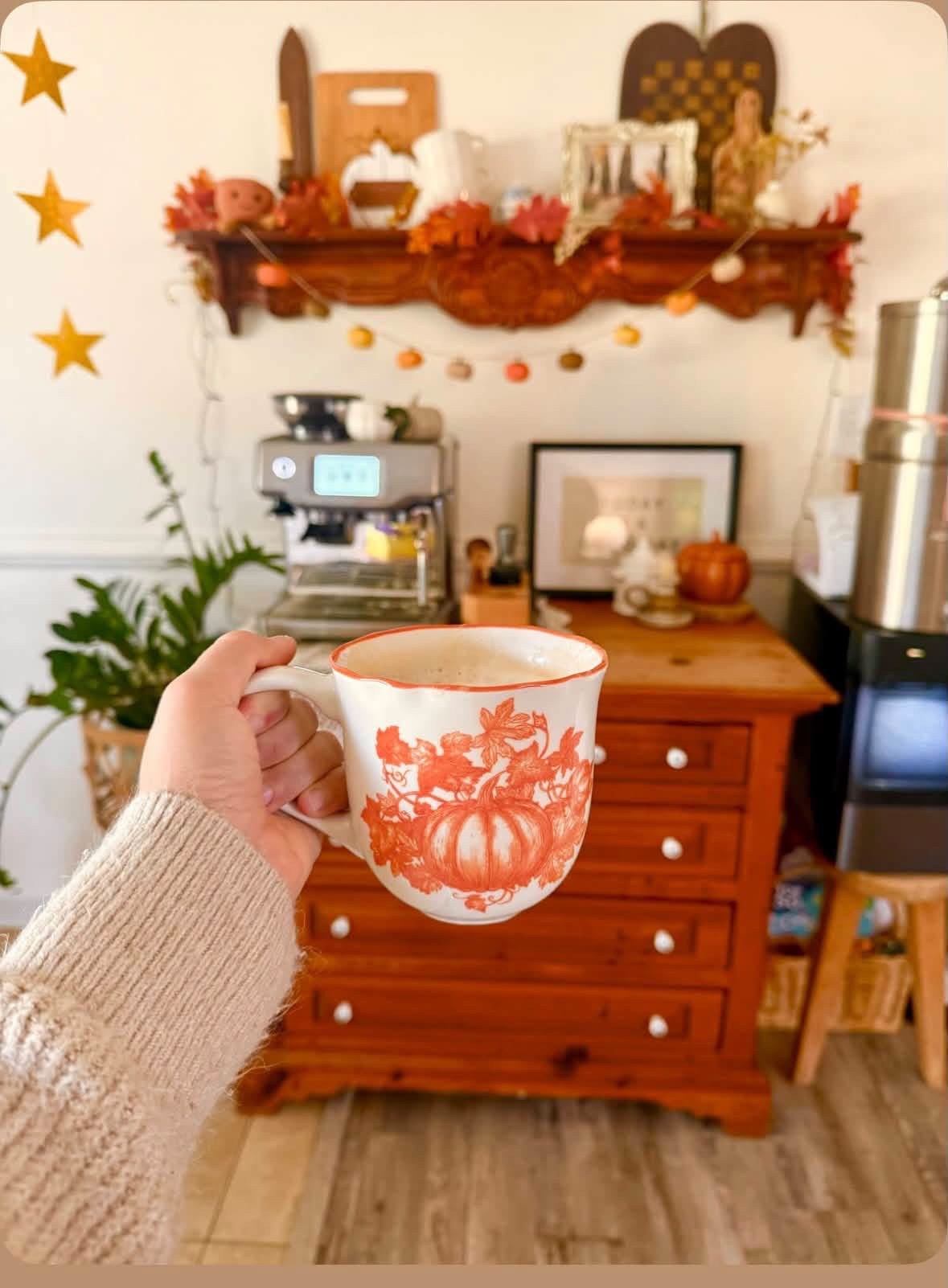 Pumpkin-patterned mug in front of a cozy autumn coffee station