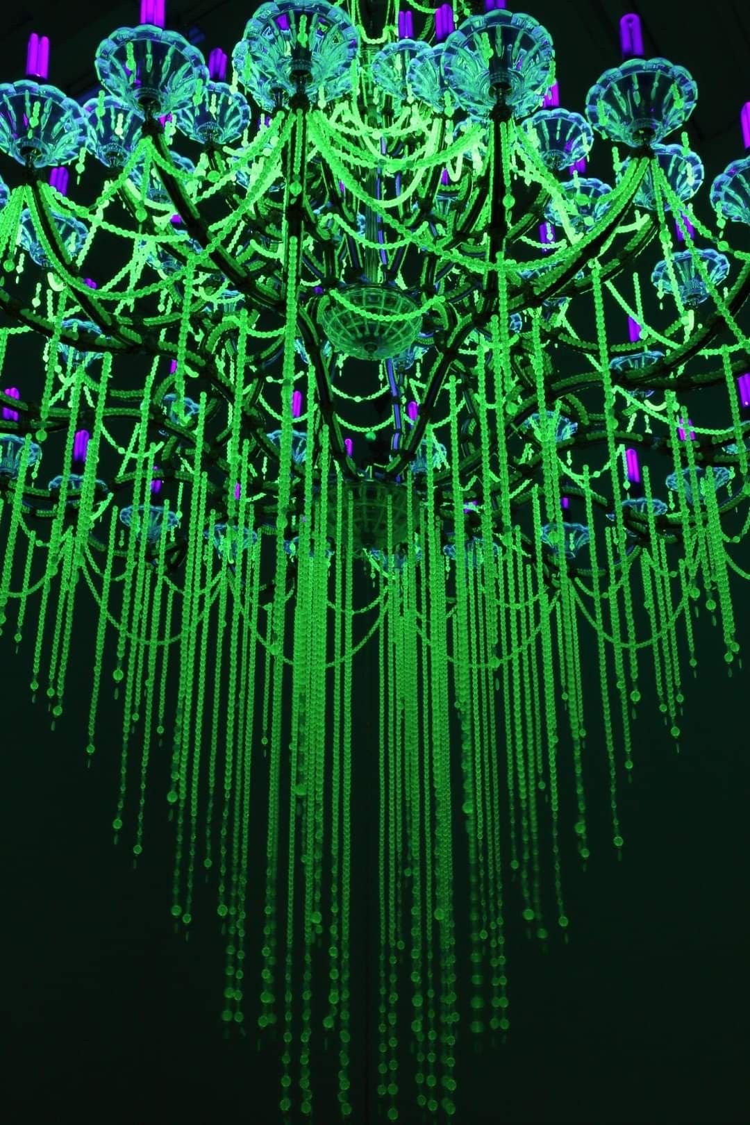 A chandelier glowing bright green under ultraviolet light
