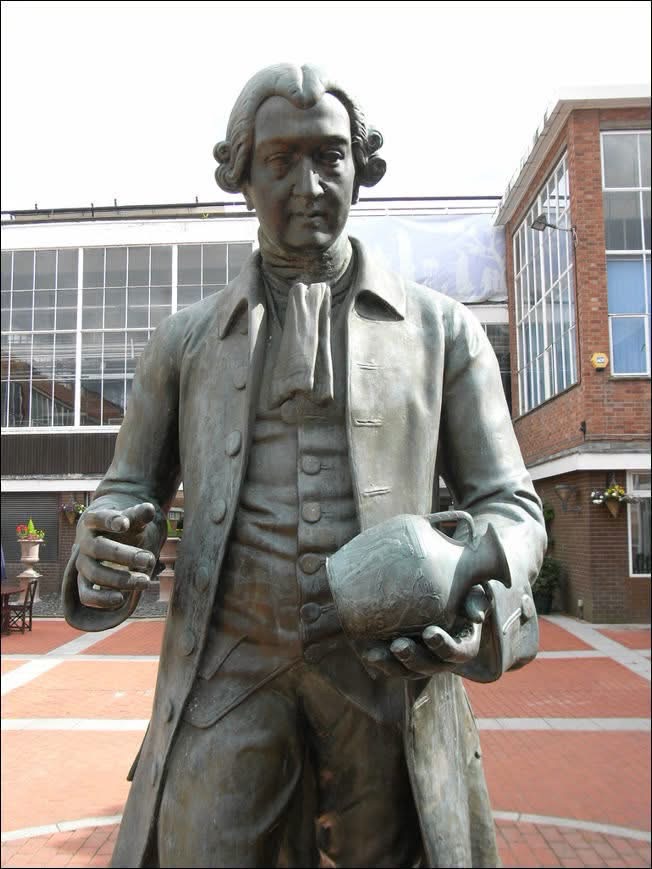 Statue of Josiah Wedgwood holding pottery outside a brick building