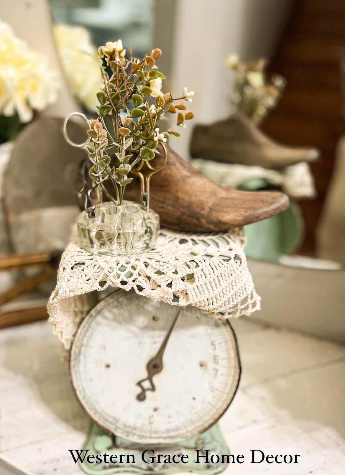 A glass flower frog holding stems on a doily covered kitchen scale