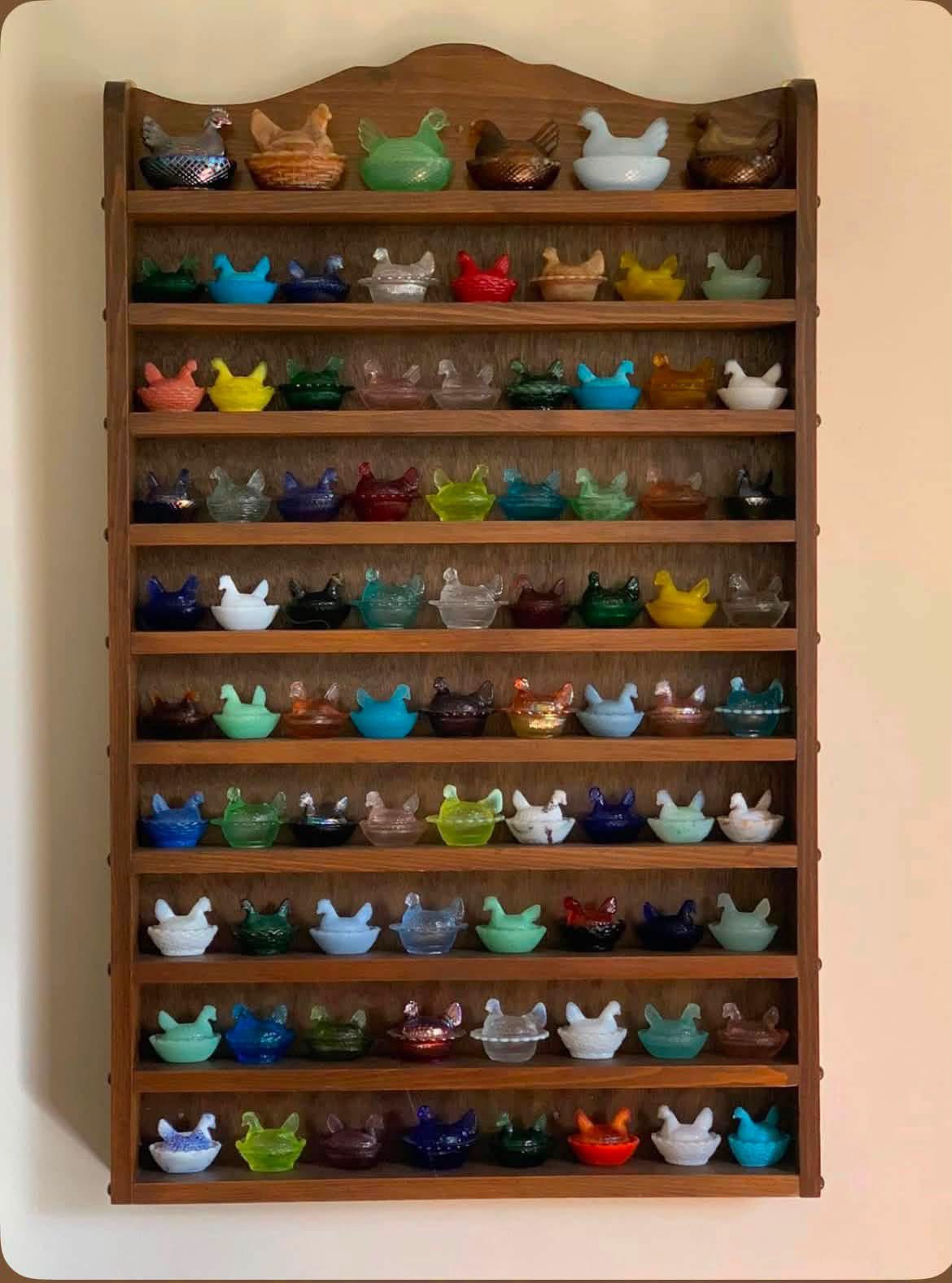 Rows of miniature glass hens in varied colors on a wooden shelf