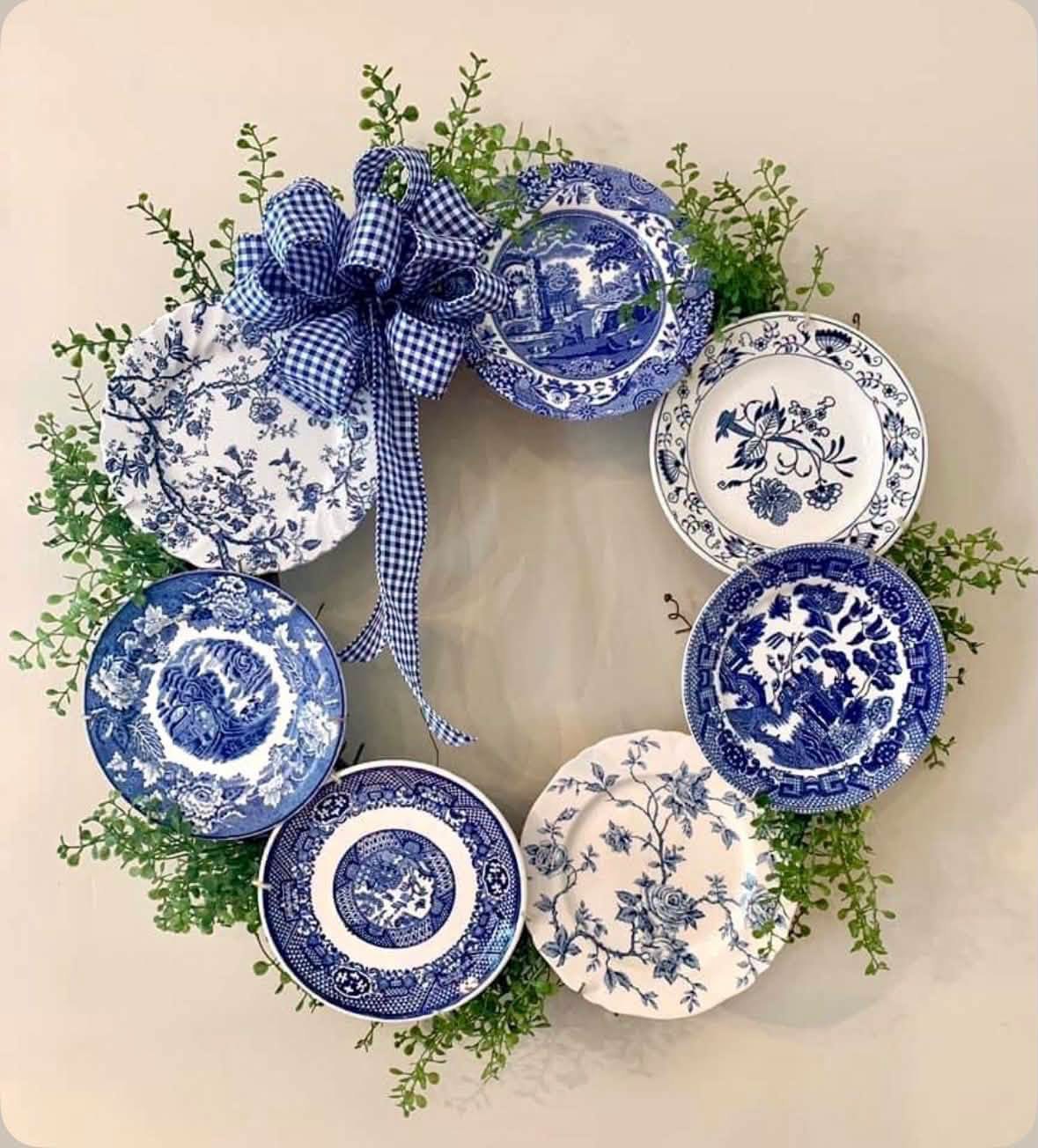 A wreath made from blue and white plates, greenery, and gingham ribbon