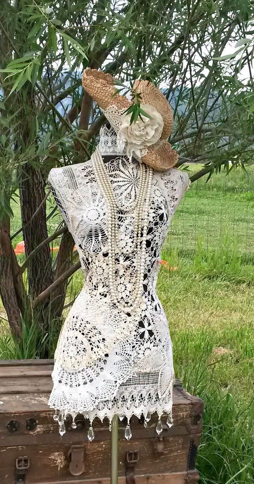 A dress form covered in lace with pearl necklaces and a straw hat