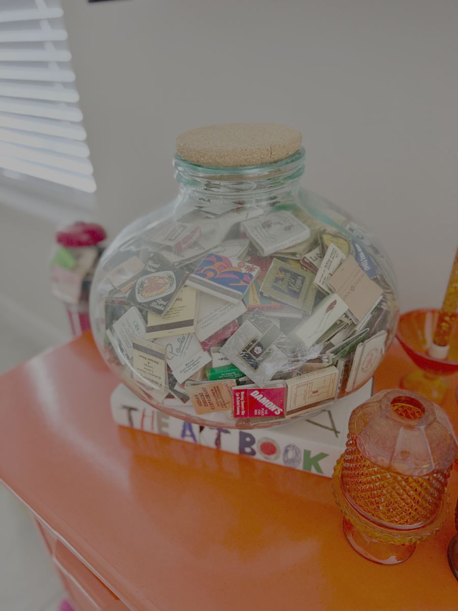 A large cork-topped glass jar filled with vintage matchbooks on an orange table
