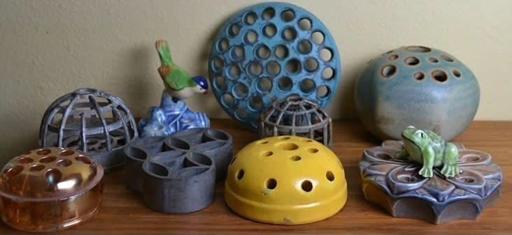 Glass, metal and ceramic flower frogs arranged on a wooden shelf