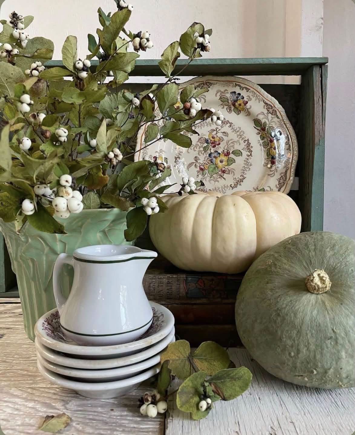 White and green pumpkins with vintage dishes and leafy branches