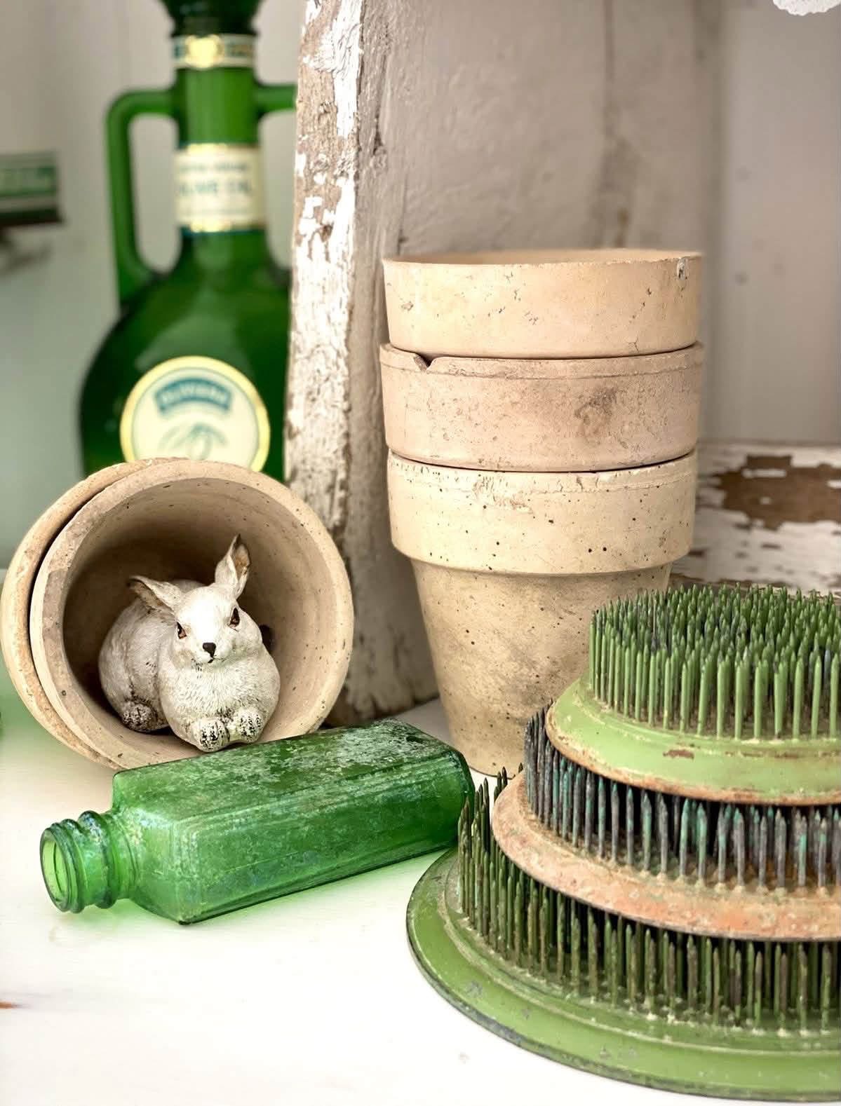 Green pin flower frogs beside cream pots and a small rabbit figurine
