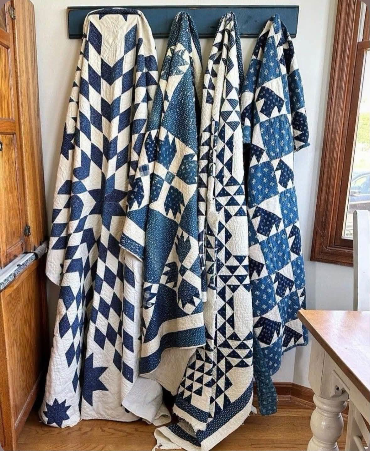 Four blue and white patchwork quilts hanging from a wall rack