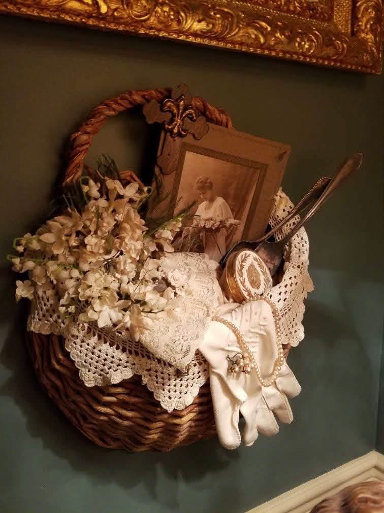 A hanging basket with lace, gloves, a portrait and vanity accessories