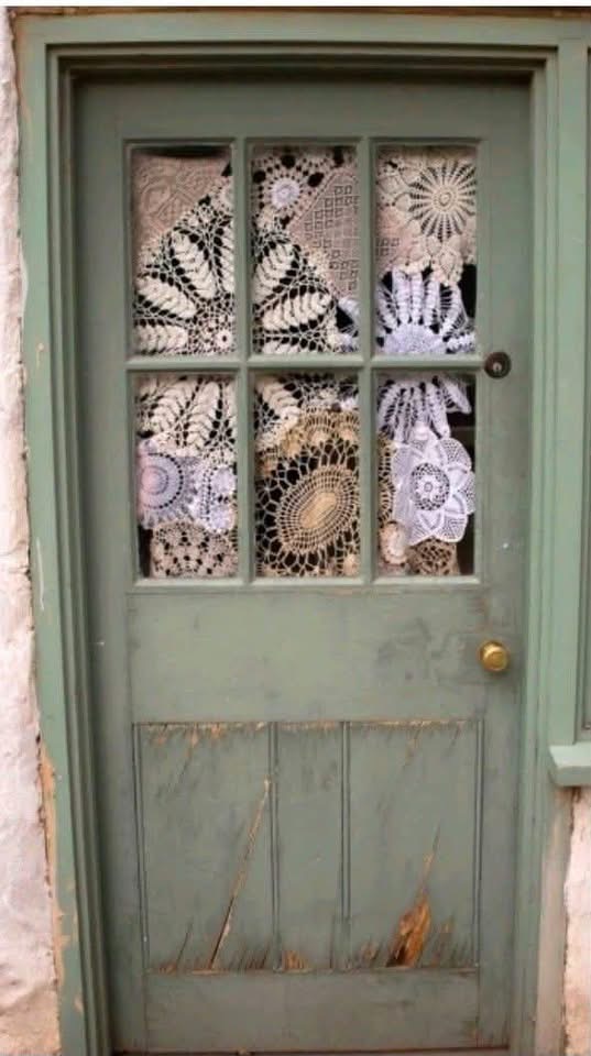 Lace doilies covering the glass panes of a weathered green door
