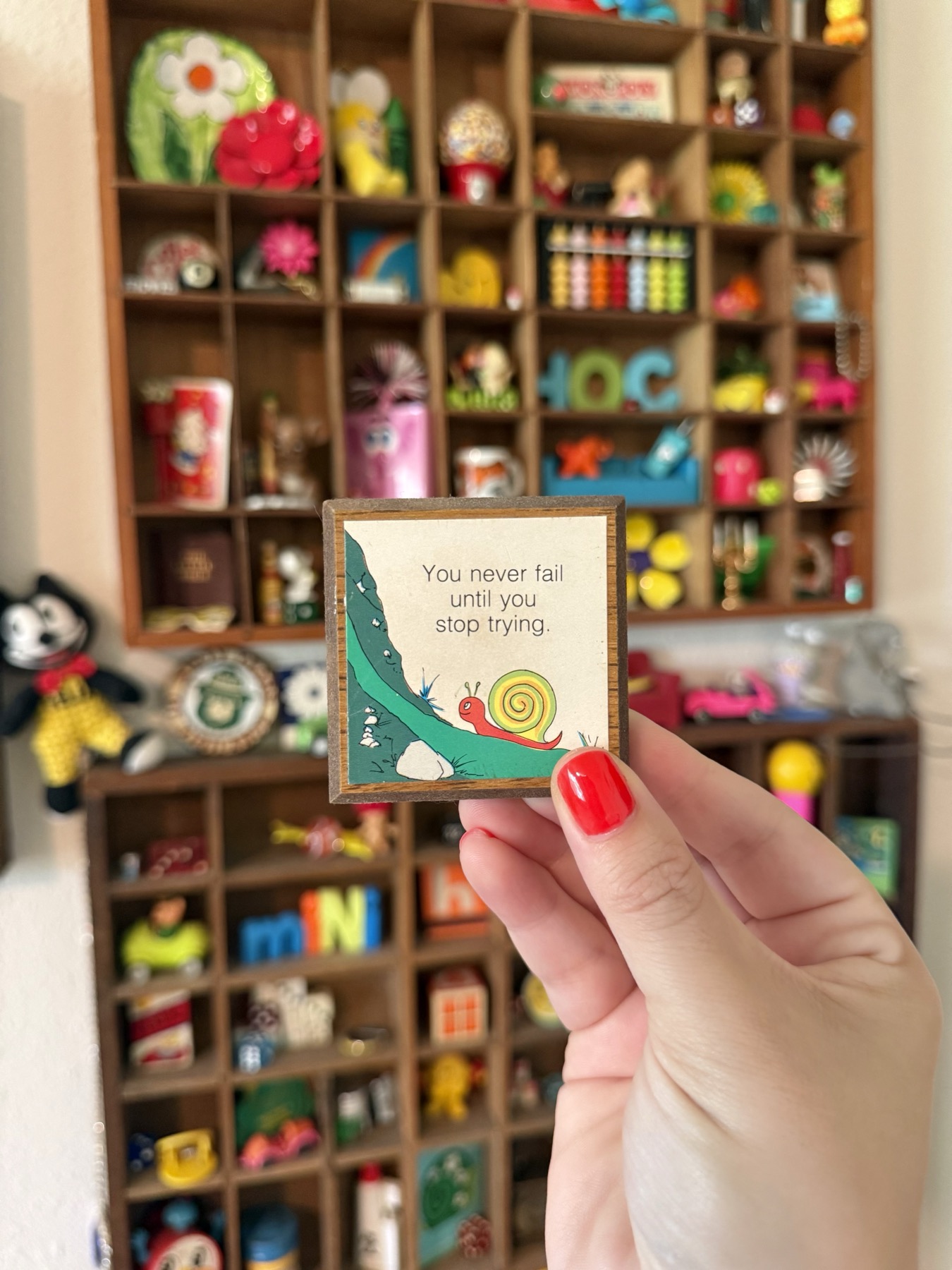 Ashley holding a miniature vintage snail wall hanging in front of colorful shelves of trinkets